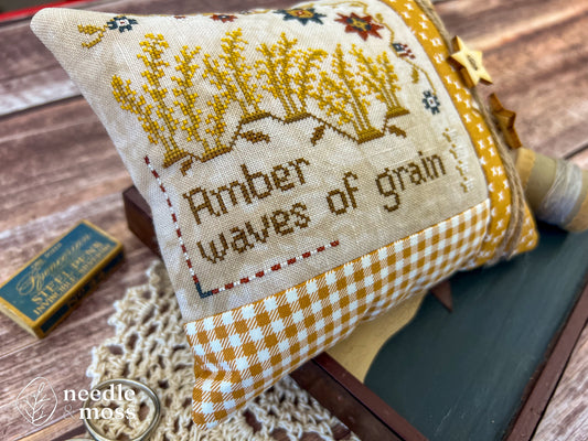 Zoomed in photo of a cross stitch pillow with Amber Waves of Grain text and motifs